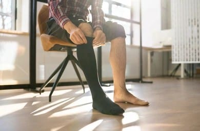 man-putting-on-medical-compression-260nw-2135166497 a man with leg pain and vein issues putting on compression socks